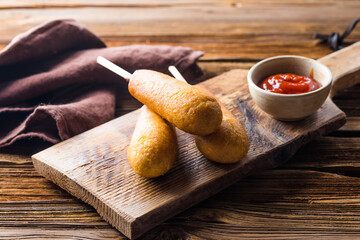 Corn dogs or sausage in roll with ketchup. Top view table scene over a wood background.