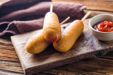 Corn dogs or sausage in roll with ketchup. Top view table scene over a wood background.
