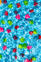 Multicolored candies under wave water, bright blue background. Summer colors concept.