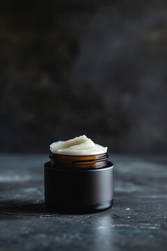 White face and body cream in a glass jar stands on a dark table. Concept of skincare cosmetics for face and body, self-care