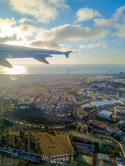 Airplane wing backlit by the rising sun flying over Lisbon with the architecture in aerial view and the Vasco da Gama bridge over the Tejo river on the horizon, PORTUGAL