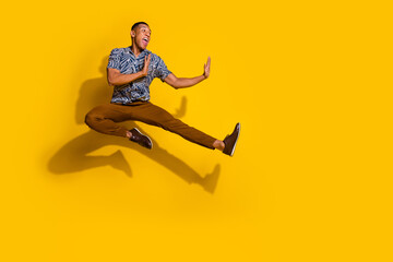 Full length photo of handsome good mood guy wear print shirt jumping high kicking empty space...