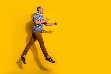 Full length photo of handsome good mood guy wear print shirt jumping high showing empty space isolated yellow color background