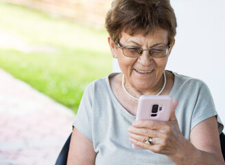One elderly woman is smiling while using her cell phone. On the video call with her family. Reading...