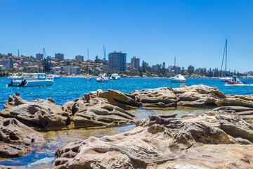 Ocean with Stones and Boats in front of Suburb of Sydney seen from Reef Bay, Sydney, Australia.
