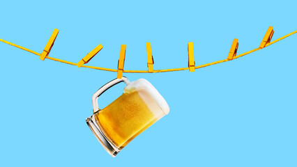 Quirky composition with mug of lager foamy beer hanging on yellow rope with clothespins against...