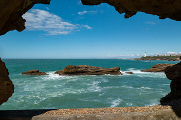 Em meio a um enorme túnel natural de rochas, alguns rochedos no mar com parte da cidade de...