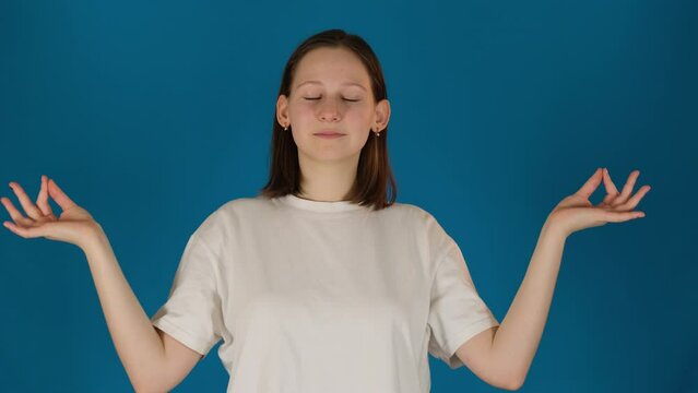 Happy lady shows meditation posture on blue background. Woman fingers delicately arrange in mudra as symbol of peace and tranquility slow motion