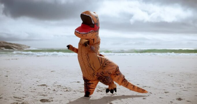 Comic, funny and dinosaur costume on beach dancing with energy for comedy joke on vacation travel. Goofy, silly and inflatable animal mascot moving, jumping and having fun by ocean on holiday.