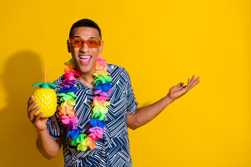 Photo of handsome good mood guy wear print shirt hawaii necklace drink cocktail showing arm empty space isolated yellow color background - obrazy, fototapety, plakaty