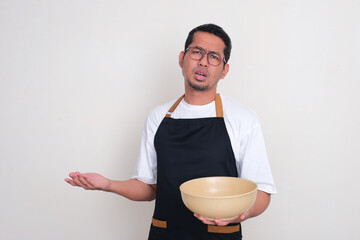 A man wearing apron showing confused expression while holding empty big serving bowl