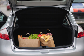 Groceries from a supermarket in a car trunk. Food delivery concept. Cruft Paper eco bags for shopping. Fresh fruits and vegetables, vegan