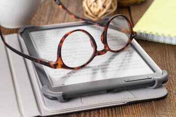 E-book and paper books on the table with a cup of coffee, a laptop and reading glasses. Concepts of...