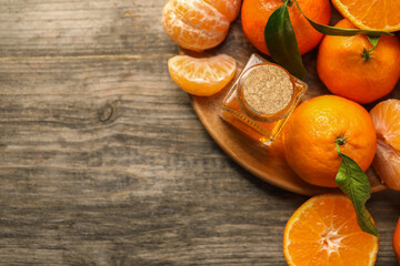 Bottle of tangerine essential oil and fresh fruits on wooden table, top view. Space for text