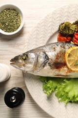 Delicious baked fish and vegetables served on wooden table, flat lay