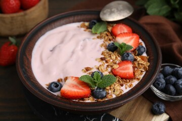 Bowl with yogurt, berries and granola on wooden table, closeup