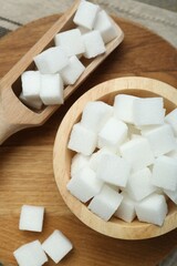 White sugar cubes in bowl and scoop on wooden board, top view
