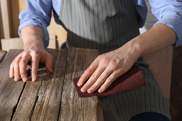 Man polishing wooden table with sandpaper indoors, closeup