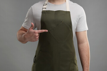 Man pointing at kitchen apron on grey background, closeup. Mockup for design