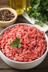 Raw ground meat in bowl, parsley, spices and oil on wooden table, closeup