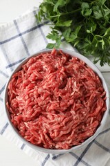 Raw ground meat in bowl and parsley on table, top view