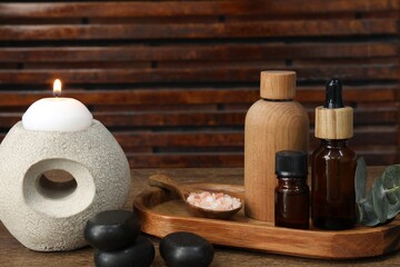 Different aromatherapy products and burning candle on wooden table