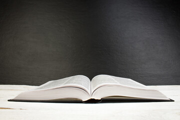 Open book on wooden deck table and black board background. Back to School. Education concept with copy space for your ad text.