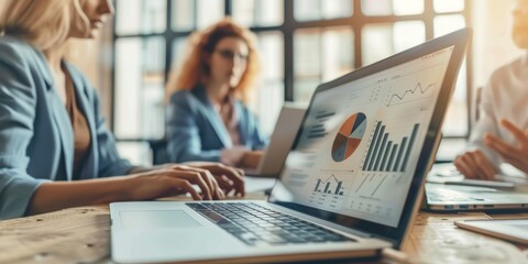 A businessman analyzes survey demographics on a laptop in an office with his coworkers. Infographic evaluation for team presentation by entrepreneur