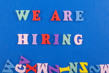 WE ARE HIRING word on blue background composed from colorful abc alphabet block wooden letters,...