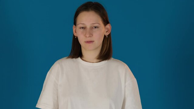 Disappointed young woman rolls up eyes posing on blue background. Pretty female model performs sarcasm standing in studio. Facial expression
