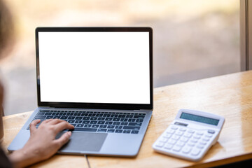 Close-up view of a laptop with a blank screen and a calculator on a wooden desk, indicating productivity and financial work.