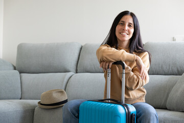 Obraz premium happy girl sitting on the sofa with her luggage and hat ready waiting to go on summer vacation
