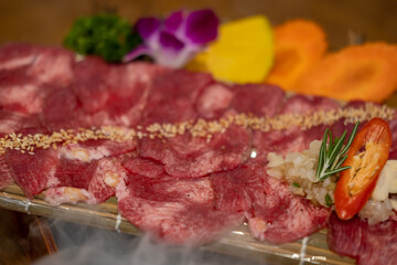 Japanese style sliced rare beef tongue meat on the plate with smoke and decoration, soft focus