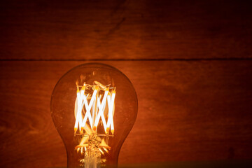 A60 E27 Edison light bulb, also known as filament light bulb on wooden background.