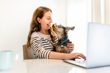 Playful dog licking woman's face, work from home concept