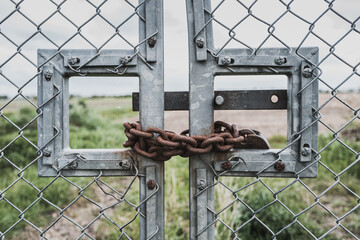 Rusty chain and padlock used to lock a farm gate which is prone to unauthorised access. The gate leads to rural land and a distant farm.