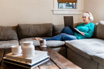 Obraz na płótnie Canvas Senior woman using laptop, surfing the internet with headphone on
