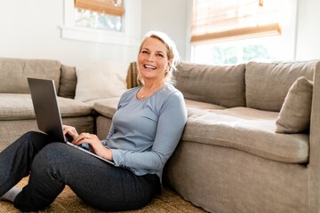 Mature woman using laptop, sitting on the living room's floor at home