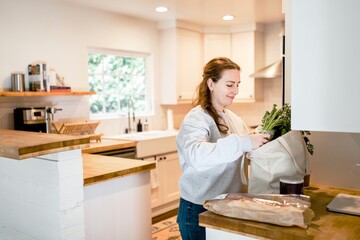 Brunette woman unpacking grocery bag in the kitchen