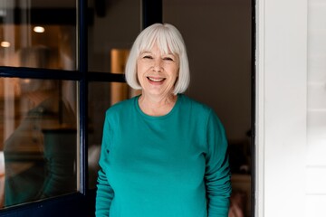 Smiling senior woman greeting guest, retirement home doorstep