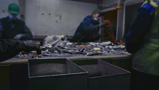 Man sorts pieces of non-ferrous metal, iron or steel on a conveyor belt with his hands or palm. Male chooses aluminum chips for recycling and remelting. Garbage factory or waste plant.
