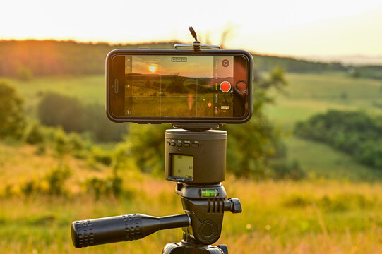 Mobile phone, smartphone on a tripod films the Beautiful sunset panorama over steppe-like landscape in Transylvania, with grasses, trees and mountains in the background, Hunedoara, Romania
