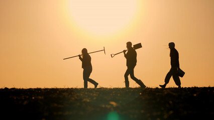 A family of farmers with working equipment walks through a field against the backdrop of a...