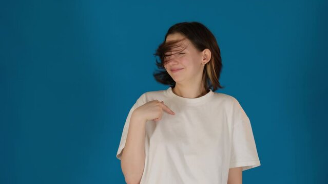 Smiling woman shows refusion with gestures and head shaking on blue background. Lady denies to take responsibility acting in studio