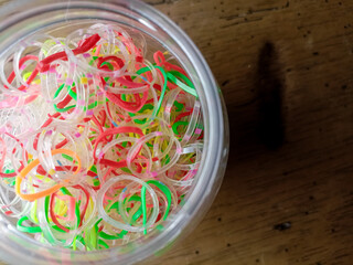 Clear glass jar full of small, kid-sized colorful rubber band hair ties. Bright vibrant colors: pink, yellow, green, purple, blue, red and orange. Container is centered on a wood background.