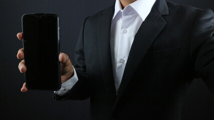 Businessman in a black suit showing smartphone with vertical blank white screen.Horizontal mockup