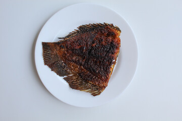 Grilled gourami fish tail, on a white plate, isolated on white background, flat lay or top view