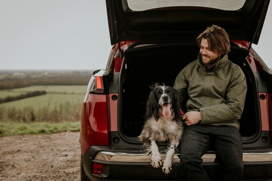 Man sitting in car trunk with dog