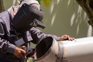 A welder wearing a protective mask grinds a metal pipe.