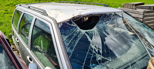 Broken windshield with a big hole in the glass on light gray station wagon car with rust and dents...